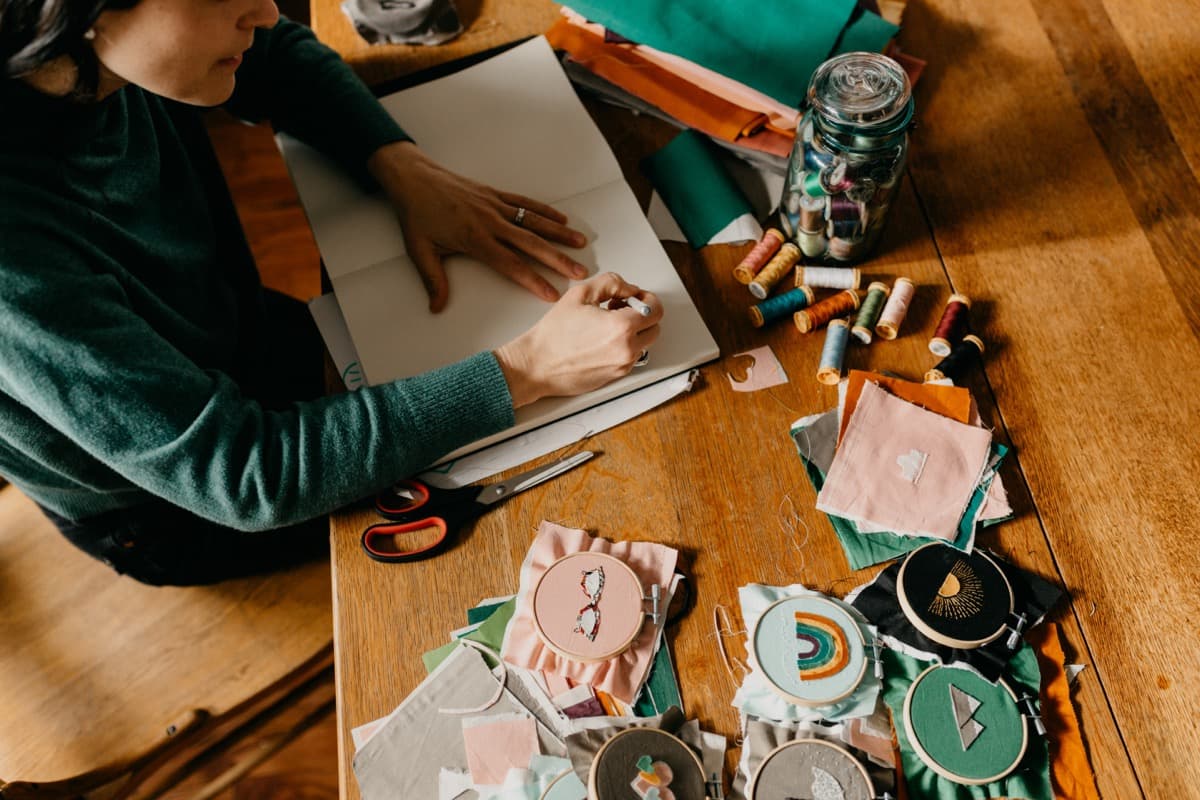 Rachel sketching and stitching badge designs at her craft table